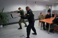 Policjant pokazuje uczniowi postawę przy mierzeniu z broni gładkolufowej