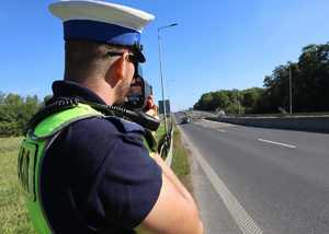 Na zdjęciu widzimy policjanta ruchu drogowego, który dokonuje pomiaru prędkości.