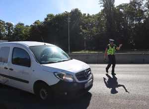 Zdjęcie przedstawia ulicę i policjanta ruchu drogowego, który wskazuje miejsce postoju nadjeżdżającemu pojazdowi.