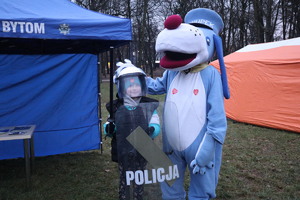 Chłopiec ubrany w kamizelkę, kask wraz z maskotką śląskiej Policji