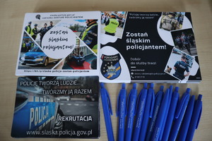 zdjęcie przedstawia ulotki &quot;Zostań Śląskim Policjantem&quot;, &quot;policję Tworzą Ludzie Twórzmy Ją Razem&quot; oraz długopisy